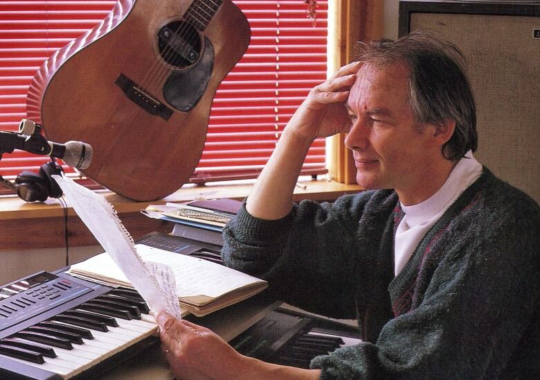 A man sits at a piano while overlooking some notes.