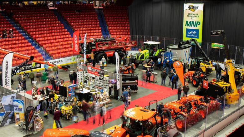 People walk through an arena filled with farming equipment.