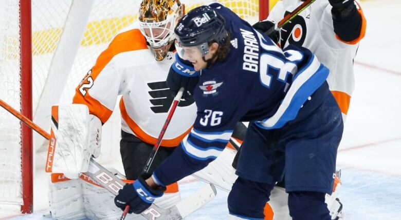 Two opposing hockey players are seen in front of a net on the rink ice.