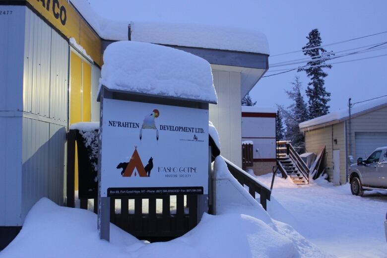 A photo of a sign in front of a pair of snow-covered buildings.