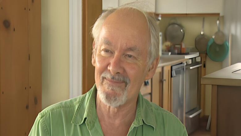 A smiling man with receding grey hair and grey facial hair.