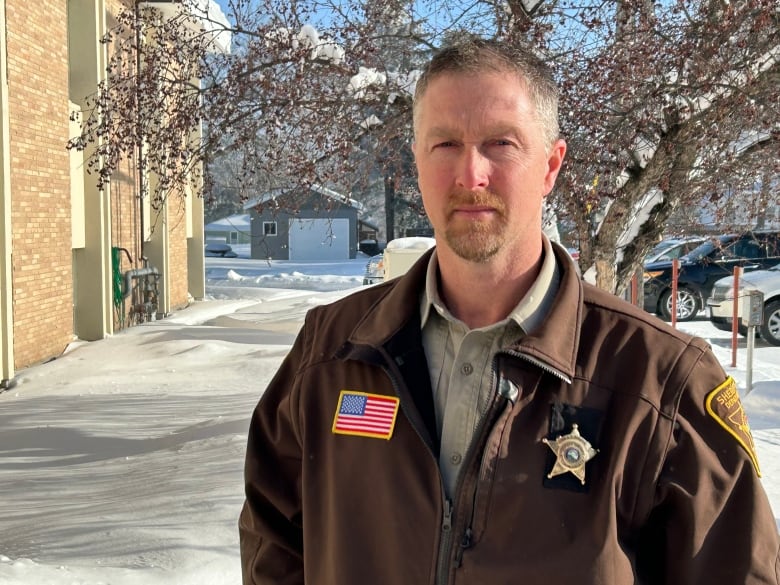 A sheriff in uniform stands outside.