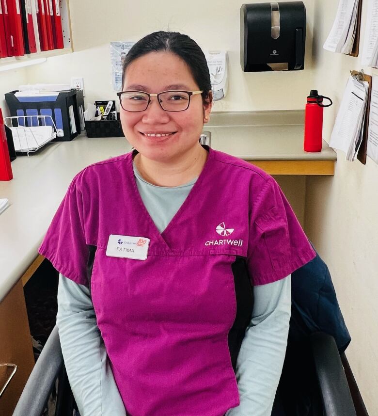 A woman sitting in an office wearing pink scrubs.