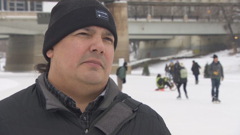 A man in a toque stands at a frozen riverfront. 