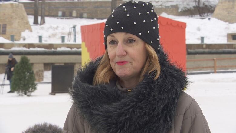 A lady in a toque stands at a frozen riverfront. 