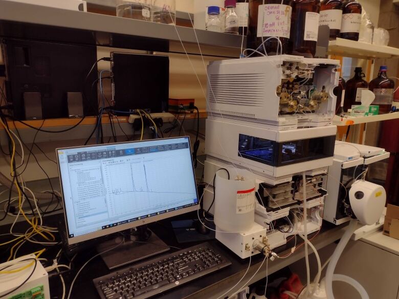 A computer in a lab next to a large printer-like device, with wires seen across the image.