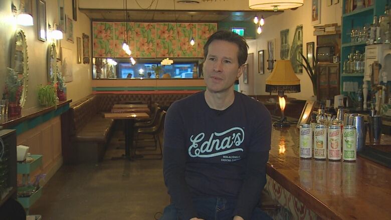 A man wearing a shirt that says 'Edna's' sits at a bar