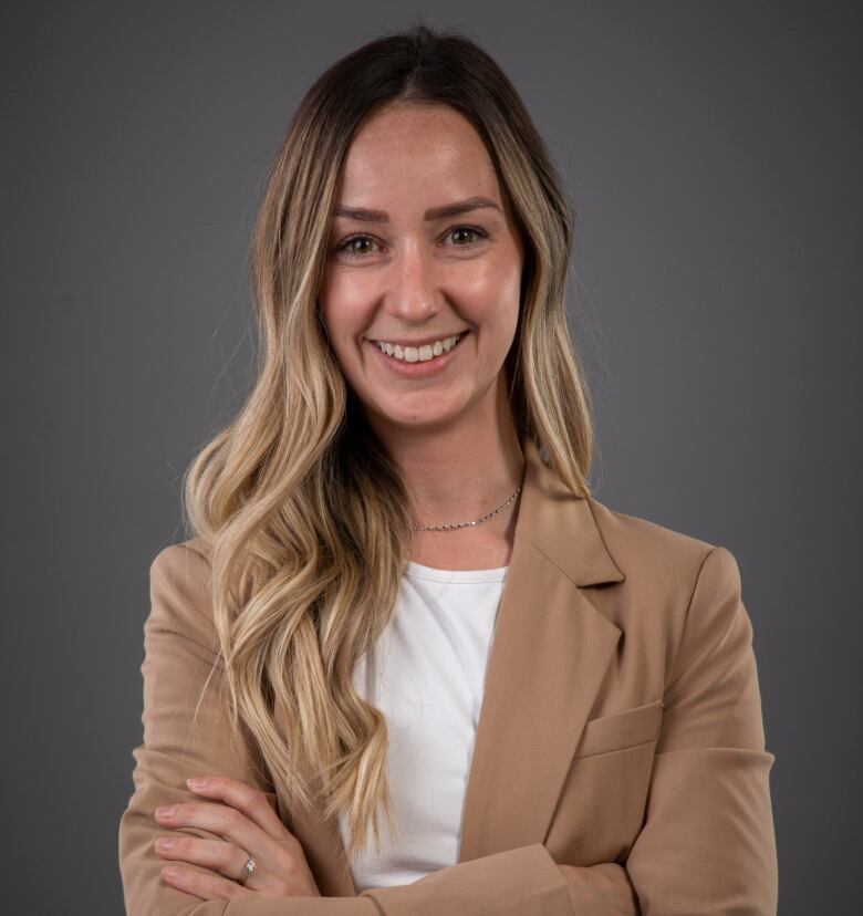 A headshot of a smiling woman stands with her arms folded.