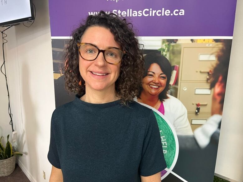 A woman with curly hair and a blue t-shirt stands in front of a purple Stella's Circle banner. 