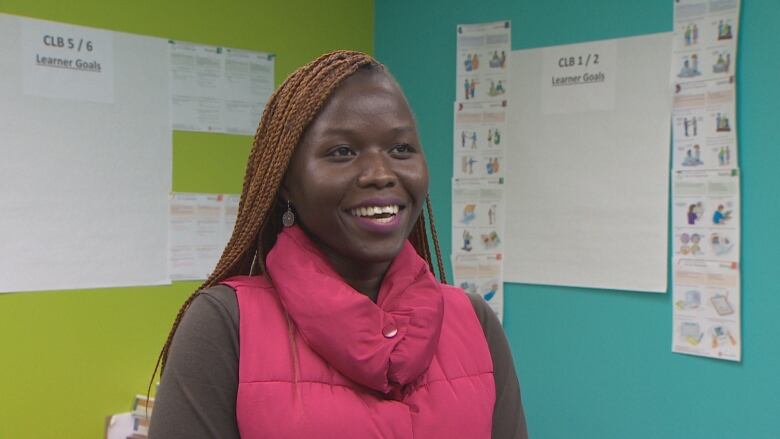 A woman who is training to be a registered nurse in Nova Scotia is shown standing in front a blue and green wall and is smiling as she is interviewed.