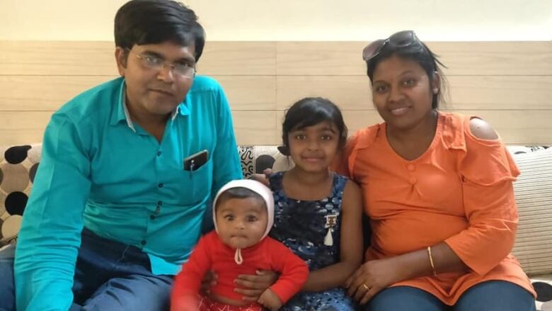 A man, a woman, a young girl and an infant boy sit together and smile.