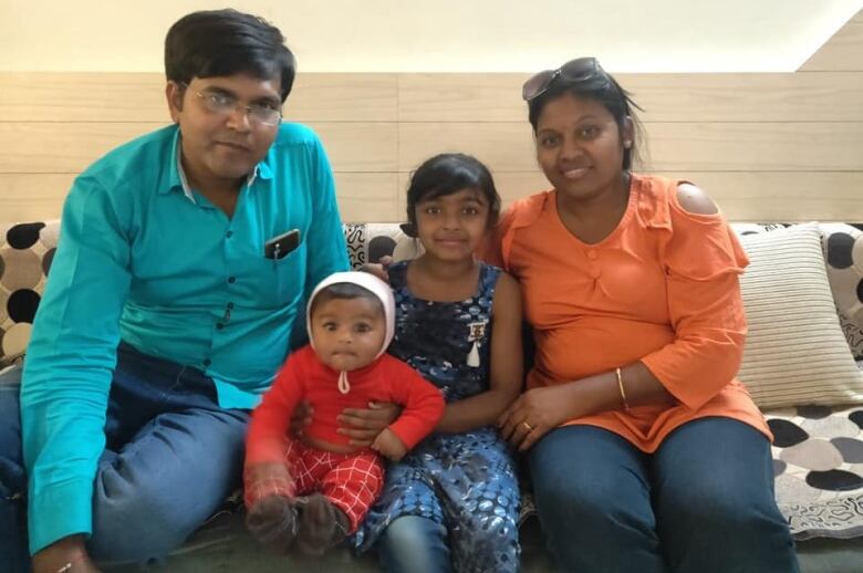 A man, a woman, a young girl and an infant boy sit together and smile.