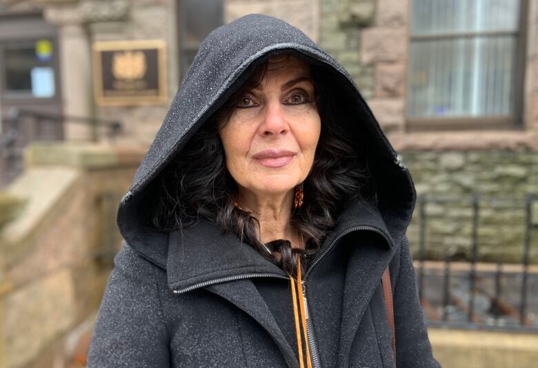 A person wearing a black hooded coat stands in front of the Supreme Court of Newfoundland and Labrador.