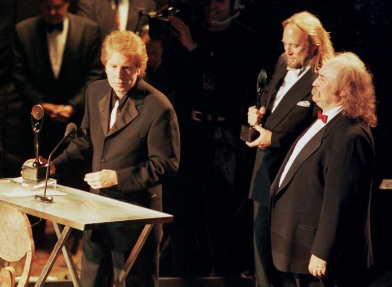 Three men in black suits on a stage are pictured from above.