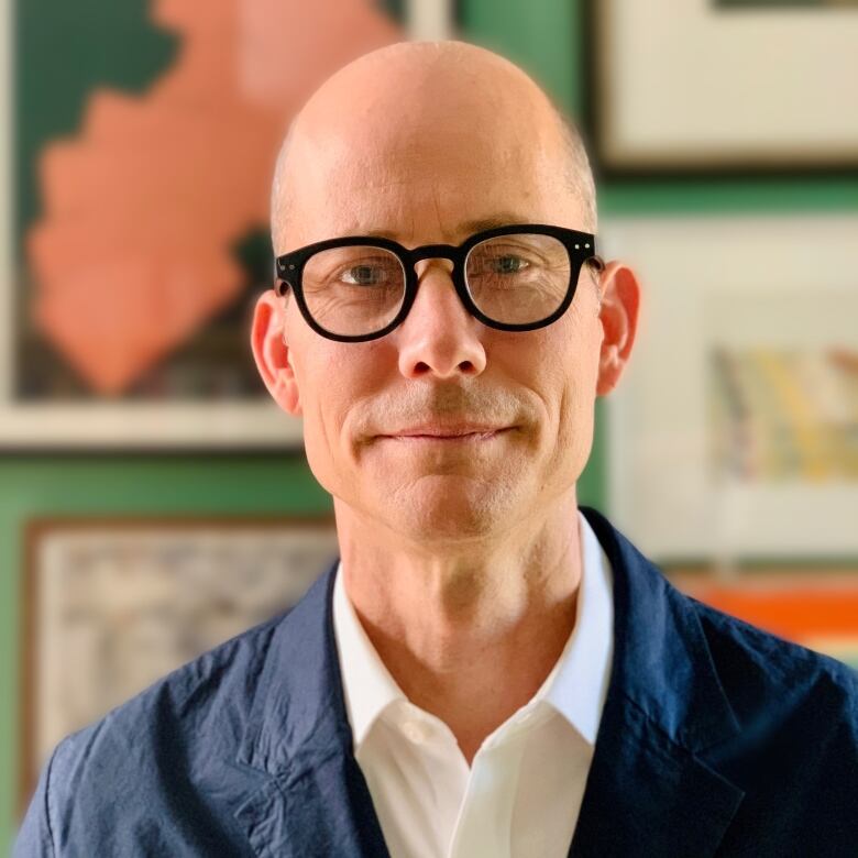 A bald spectacled man in a blue suit smiles.