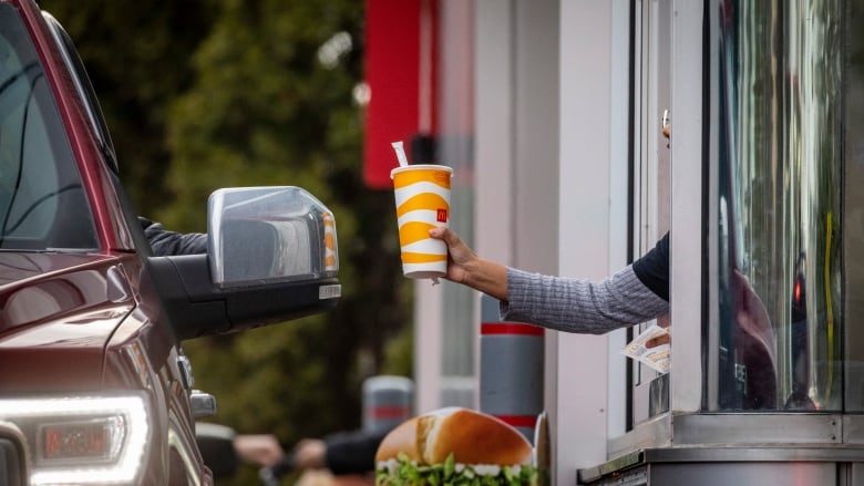 A food service worker hands a McDonald's branded cup to a driver through a drive-thru window.