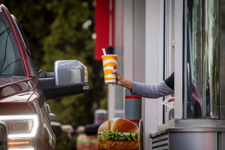 A food service worker hands a McDonald's branded cup to a driver through a drive-thru window.