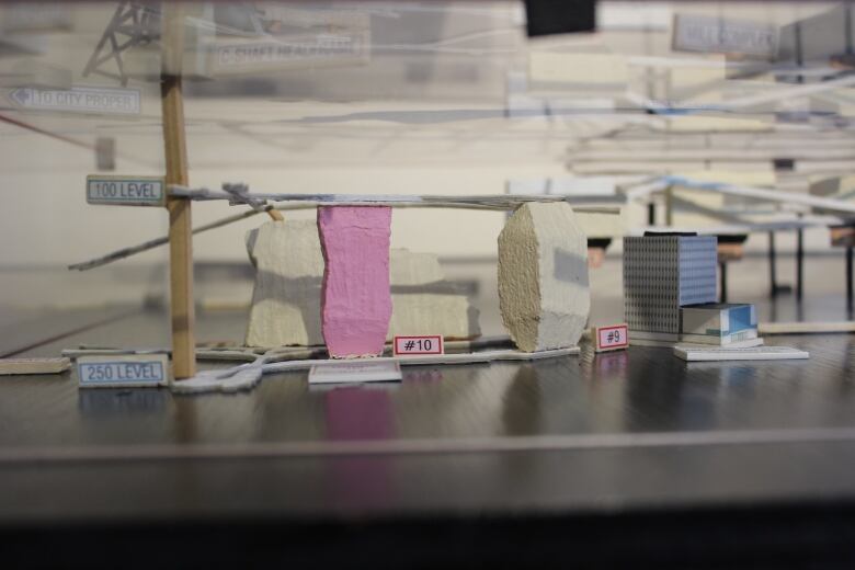 A model of mine chambers below ground. In the foreground, one chamber is pink, one chamber is white, and there's a model of a building sitting next to them. 