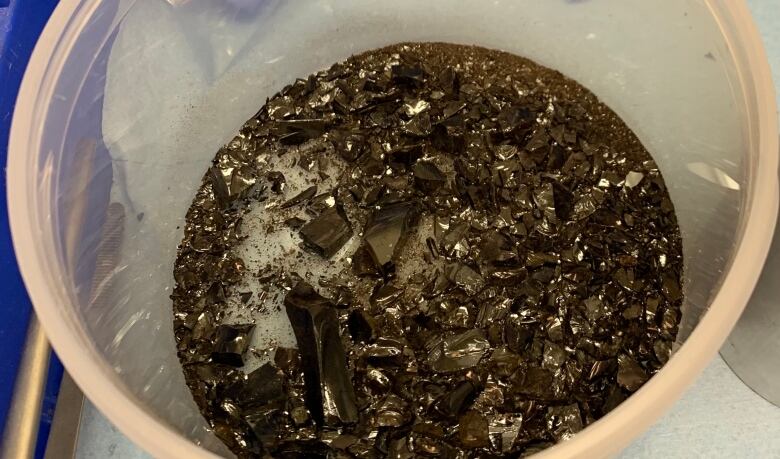 A clear bucket with hunks of black broken glass in the bottom.