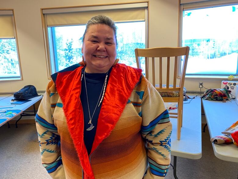 A portrait of a woman smiling. She's wearing a tradditional Indigenous coat.