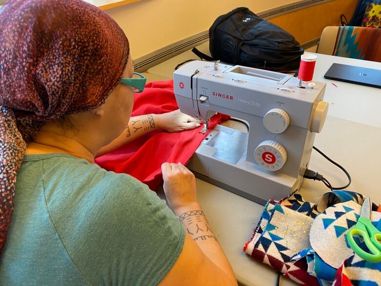 A woman seen from behind sitting at a table and working a sewing machine.