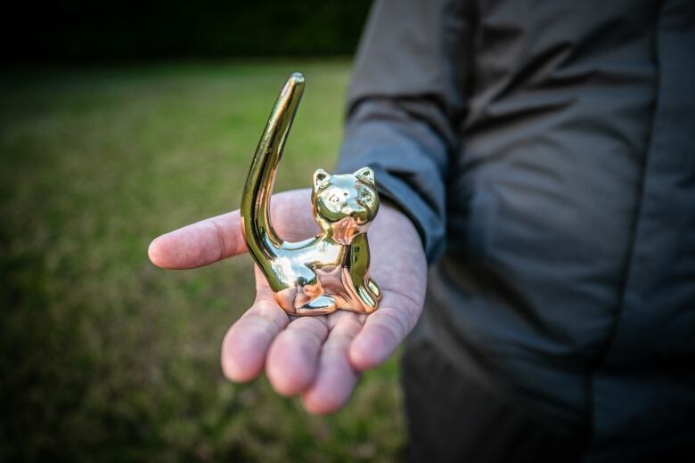 A man holds a cat figurine in a closeup outside in Victoria.