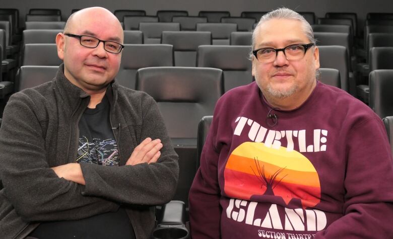 Two men pose for a photo in movie theatre seats.