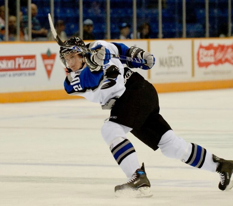 A hockey player in a blue and white uniform is seen on the ice with his stick in the air