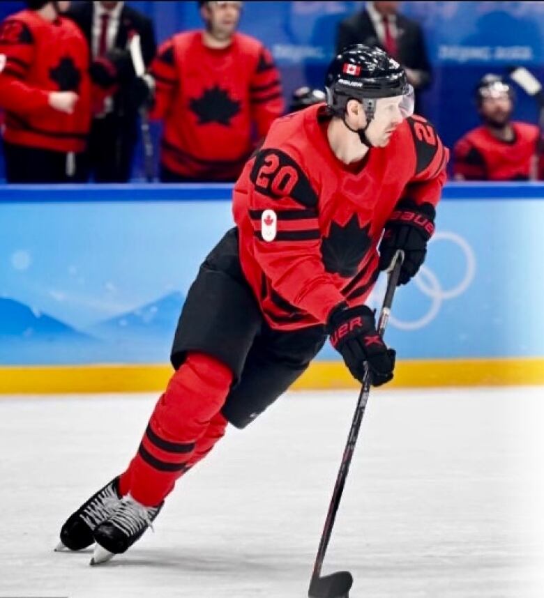 A hockey player in a red Canadian uniform on the ice with teammates on the bench in the background