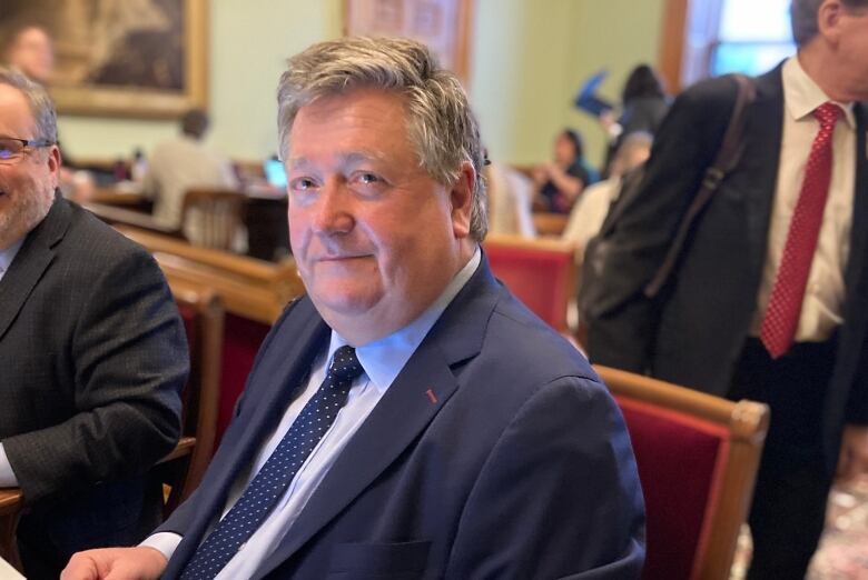 A man in suit and tie seated at a table in the New Brunswick legislature.