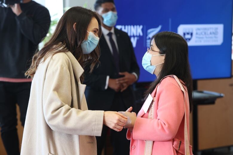 Two women in face masks hold hands and look each other in the eyes. 