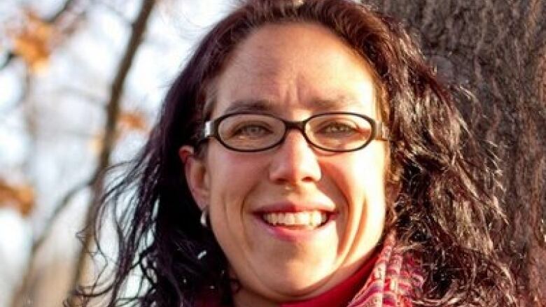 Portrait of woman in bright red sweater and purple scarf. She's standing outside by some trees.