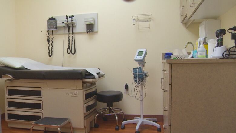 A doctor's office room with a bed, blood pressure cuff on the wall, and cabinets against the right wall.