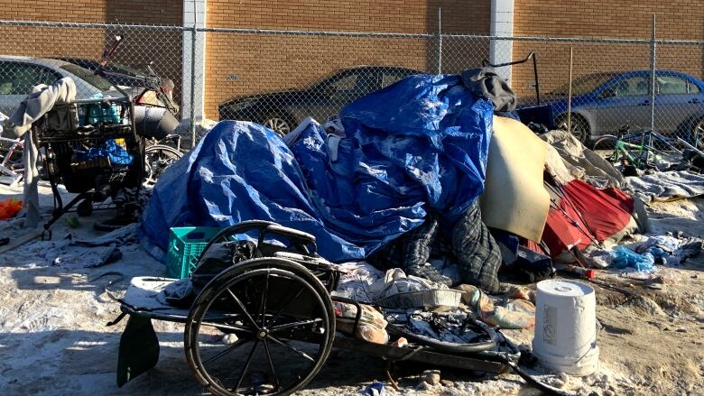 A tent is covered in tarps, and surrounded by carts, buckets and other debris. 