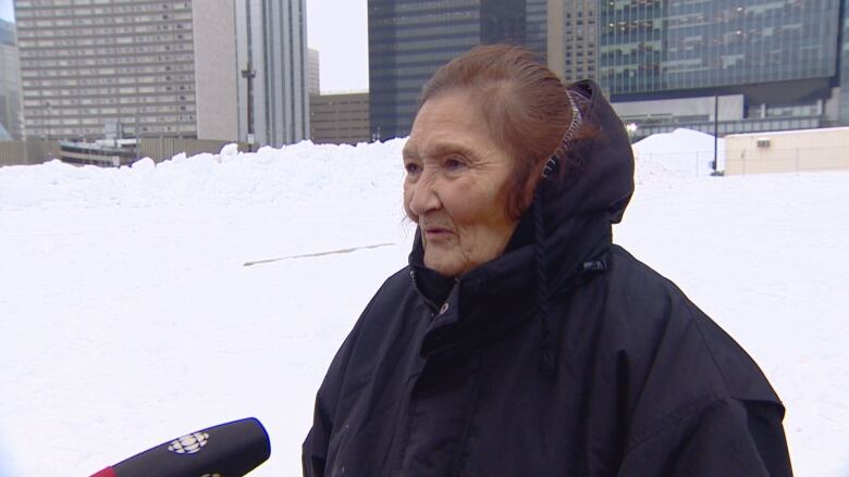 A woman wearing a winter coat speaks into a microphone.