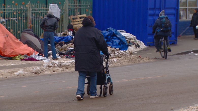 A woman pushing a walker walks down a street. 