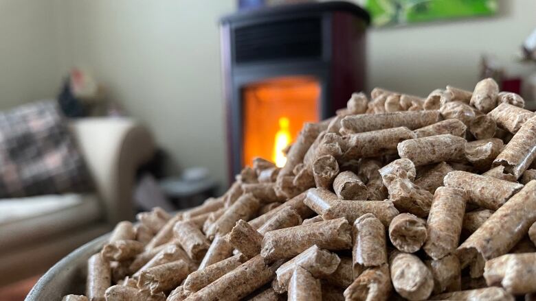 A pile of wood pellets in the foreground with a burning pellet stove in the background.