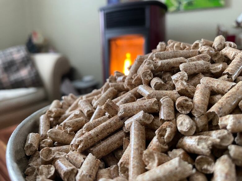 A pile of wood pellets in the foreground with a burning pellet stove in the background.