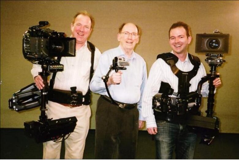 Three smiling white men carrying camera equipment.