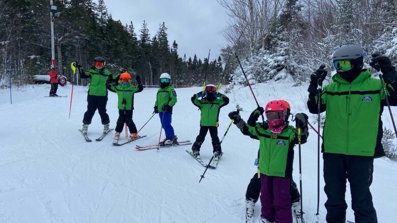 Six skiiers dressed in green snow jackets and wearing skis pose for a photo on a snow covered mountain. 