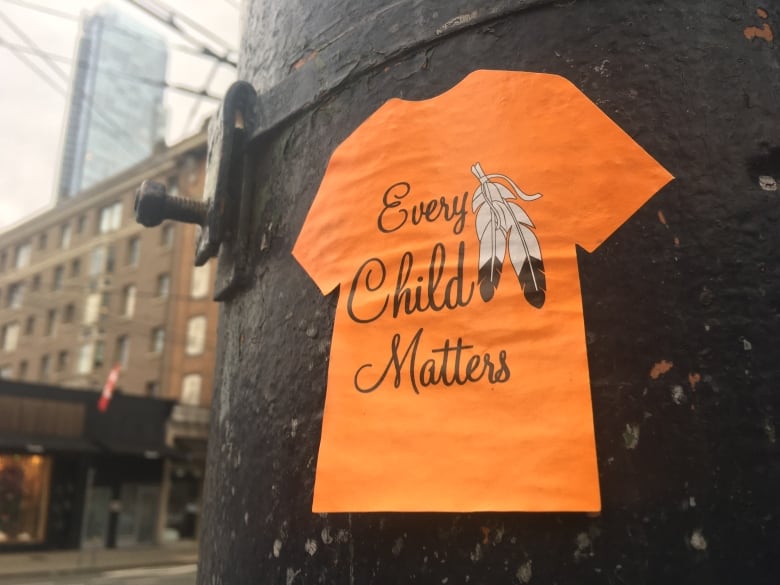 A sticker of an orange t-shirt with the words 'Every Child Matters' on it affixed to a lamp post.