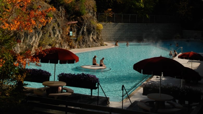 A pool at the side of a mountain is pictured with leaves turning orange on the trees.