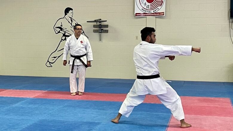 Joshbir Roy practices kata, a type of karate at Charlottetown Martial Arts. He is wearing a brown belt and punching forward as his instructor stands watching. 