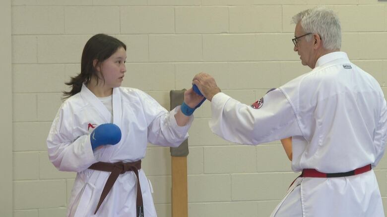 Karate student Bria Wong trains with her coach Collin Affleck. Wong has a brown belt, low ponytail and blue gloves. She punches forward as Affleck grabs her hand.