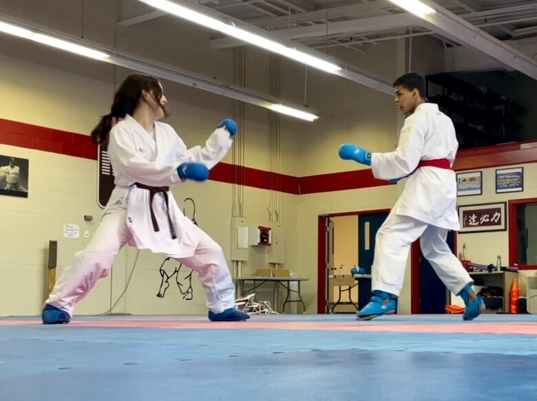 Bria Wong and Sarvessh Dhanasekar face off against one another in a practice round at Charlottetown Martial Arts. Both are dress in white standing in a wide leg stance waiting for their opponent to strike. 