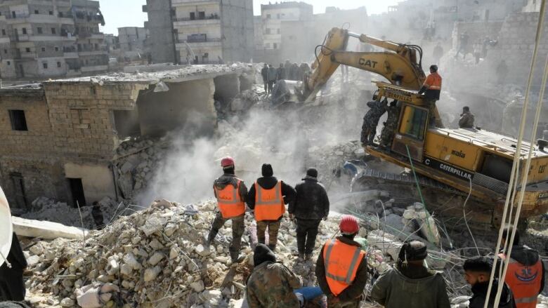 Rescuers stand on the rubble of a collapsed building.