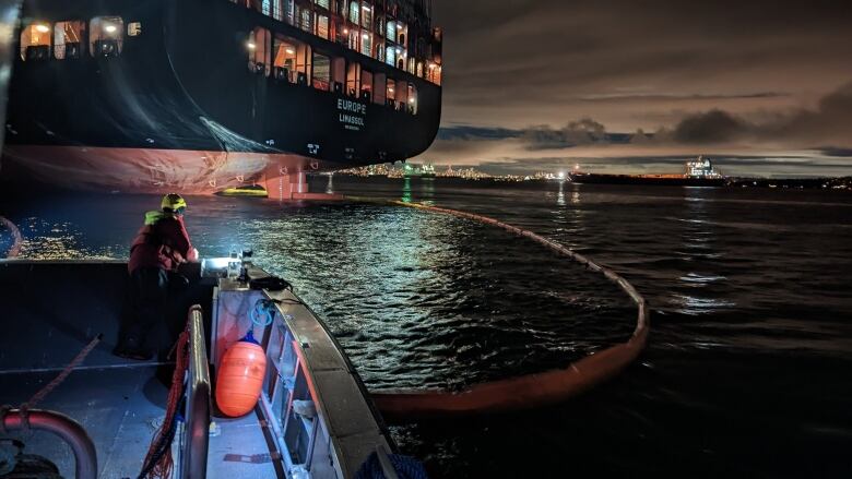 A nighttime picture of a boom containing an oil spill from a large container ship off in the distance.