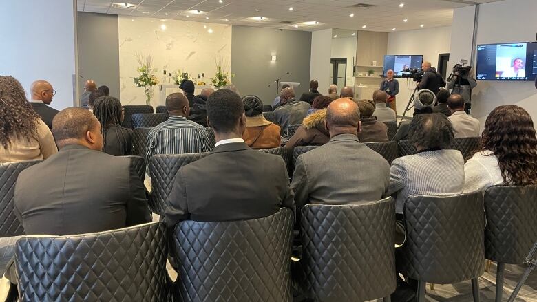 A photo taken from behind of peop;e sitting in chairs at funeral service. 