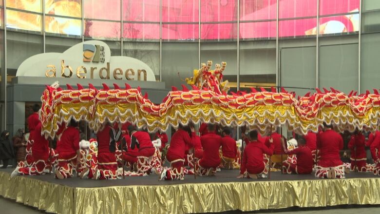 People dressed in red hold up a long red and gold dragon on a stage in Aberdeen Centre. 