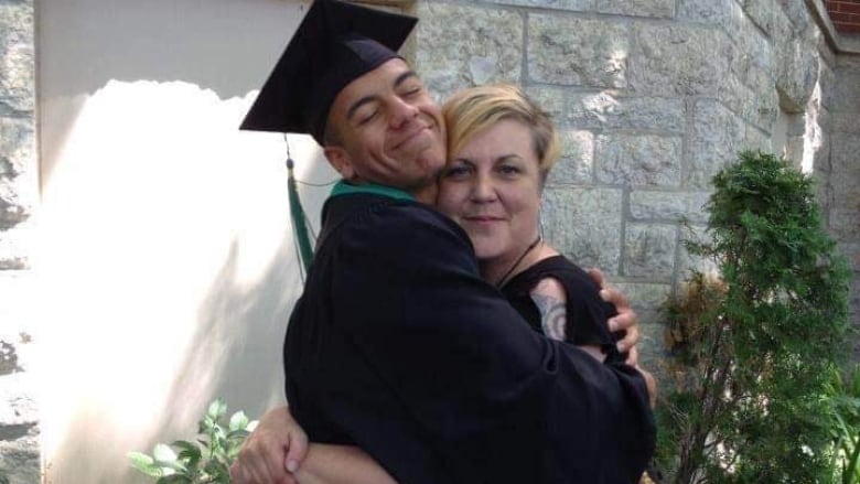 A man in a cap and gown hugs a woman with blonde hair.